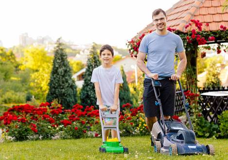 Father and son mowing backyard together. Standing and smiling.